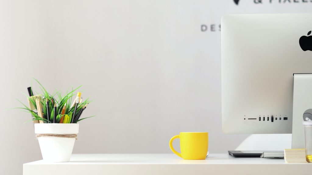 desk with a computer, pot of pens and a mug